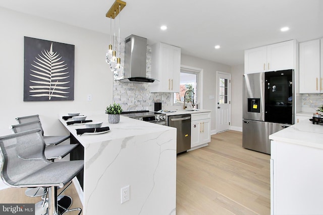 kitchen featuring white cabinets, hanging light fixtures, wall chimney exhaust hood, and stainless steel appliances