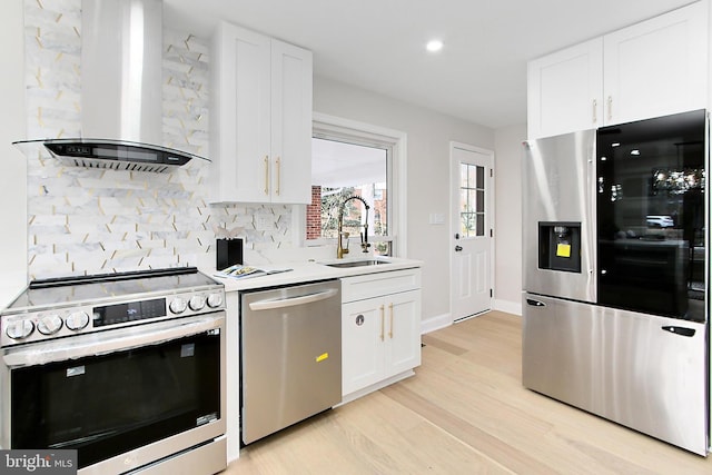 kitchen with white cabinets, sink, wall chimney exhaust hood, appliances with stainless steel finishes, and light hardwood / wood-style floors