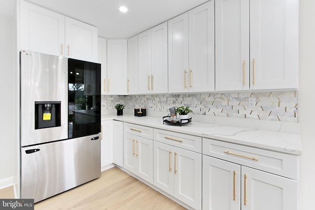 kitchen with light wood-type flooring, tasteful backsplash, light stone counters, white cabinets, and stainless steel fridge with ice dispenser