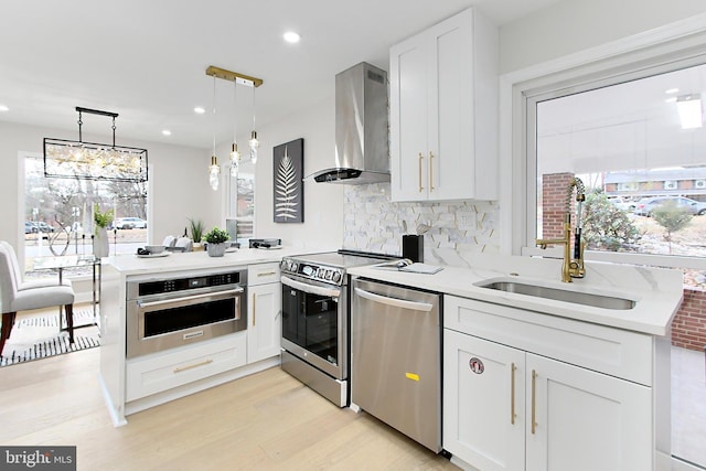 kitchen featuring pendant lighting, white cabinets, wall chimney range hood, appliances with stainless steel finishes, and kitchen peninsula