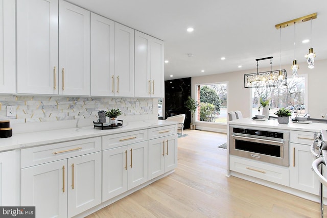 kitchen with decorative backsplash, light stone countertops, stainless steel oven, white cabinets, and hanging light fixtures