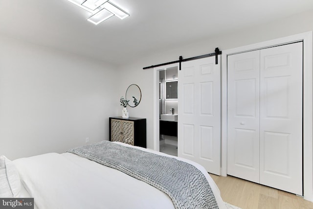 bedroom with sink, a barn door, ensuite bathroom, a closet, and light wood-type flooring