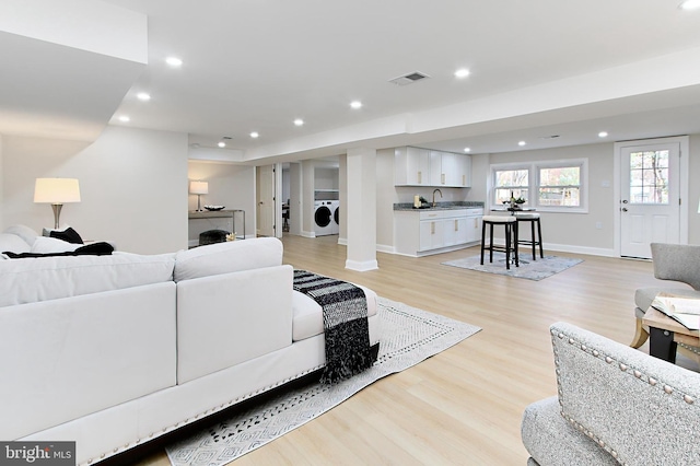 living room featuring separate washer and dryer, light hardwood / wood-style flooring, and sink