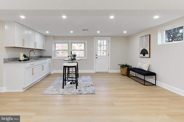 kitchen featuring white cabinetry, light stone counters, a kitchen bar, and light wood-type flooring