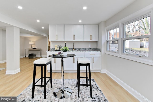 kitchen featuring white cabinets, a kitchen bar, light hardwood / wood-style flooring, and sink