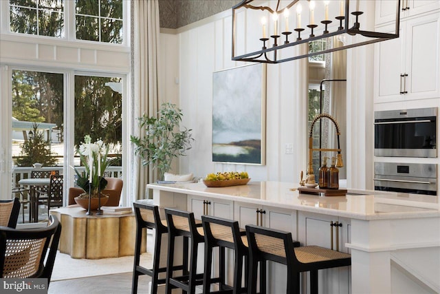 bar with double oven, white cabinetry, light stone counters, and plenty of natural light