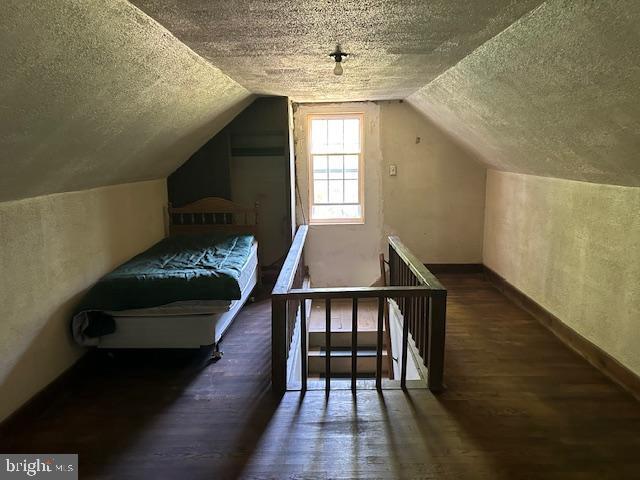 bedroom with a textured ceiling, dark hardwood / wood-style flooring, and vaulted ceiling