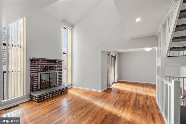 unfurnished living room featuring high vaulted ceiling, light hardwood / wood-style floors, and a brick fireplace