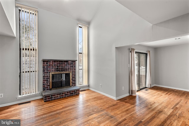 unfurnished living room featuring plenty of natural light, light hardwood / wood-style floors, vaulted ceiling, and a brick fireplace