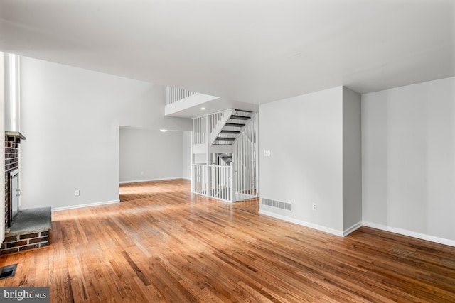 unfurnished living room featuring wood-type flooring and a brick fireplace