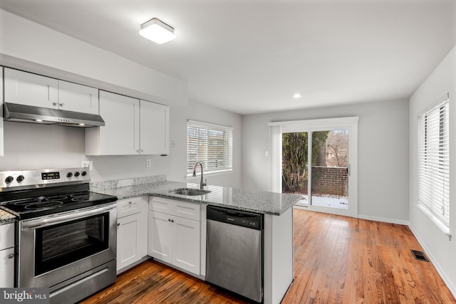 kitchen featuring sink, light stone countertops, appliances with stainless steel finishes, white cabinetry, and kitchen peninsula