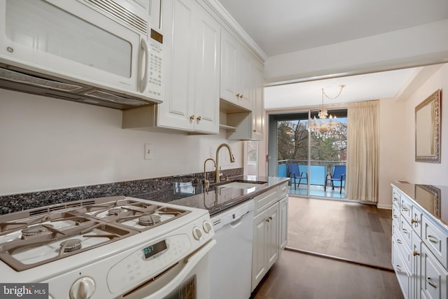 kitchen with white appliances, hanging light fixtures, an inviting chandelier, white cabinets, and sink