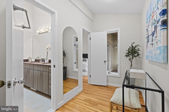 corridor featuring light wood finished floors, arched walkways, baseboards, and a sink