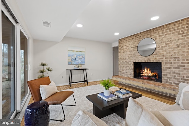 living area featuring visible vents, wood finished floors, recessed lighting, baseboards, and a brick fireplace