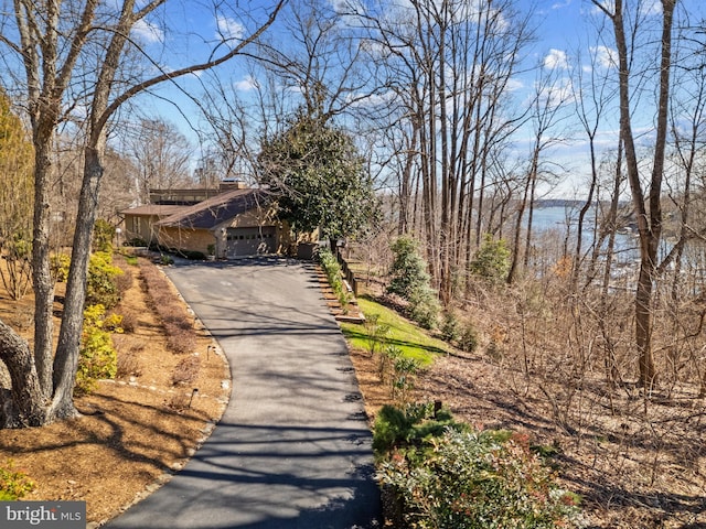 view of front of property with aphalt driveway, a water view, a garage, and a chimney