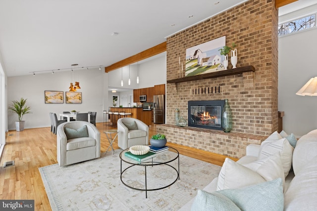 living room with visible vents, light wood finished floors, vaulted ceiling with beams, a fireplace, and rail lighting