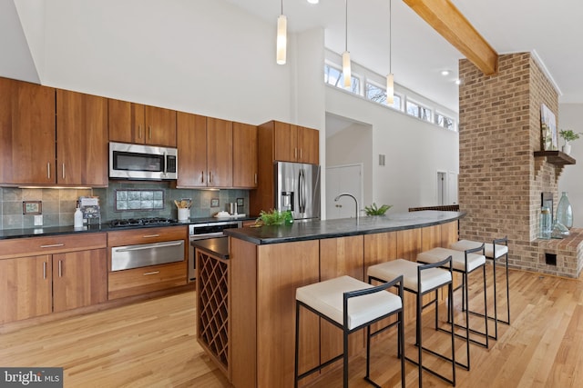 kitchen with a warming drawer, light wood-type flooring, beam ceiling, dark countertops, and stainless steel appliances