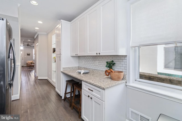 kitchen with white cabinets, ornamental molding, a wealth of natural light, and stainless steel fridge