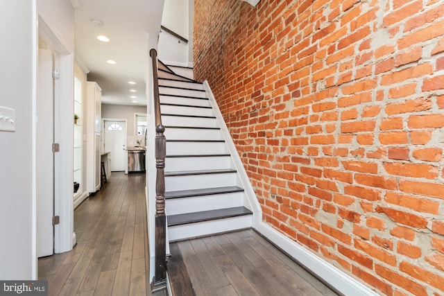 stairs featuring hardwood / wood-style floors and brick wall