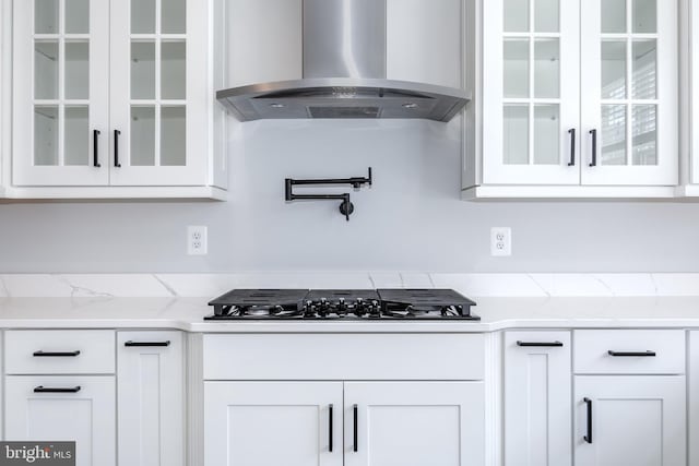 kitchen with black gas cooktop, white cabinets, light stone countertops, and wall chimney range hood