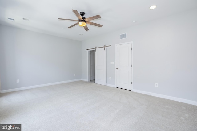 unfurnished bedroom featuring a barn door, light colored carpet, and ceiling fan