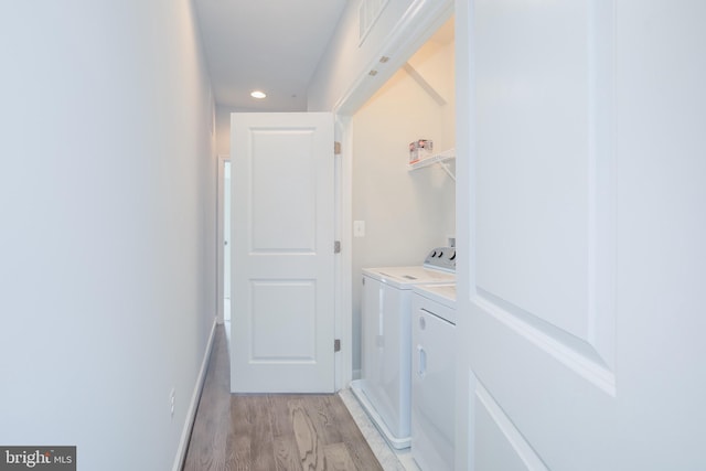 clothes washing area with washing machine and dryer and light wood-type flooring