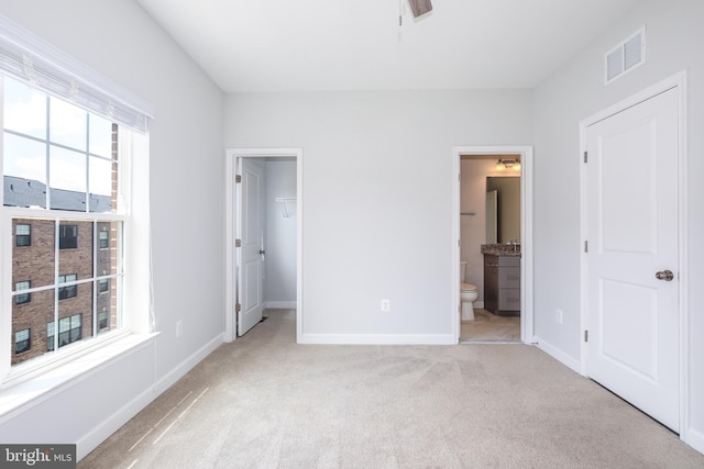 unfurnished bedroom with a walk in closet, connected bathroom, light colored carpet, and a closet