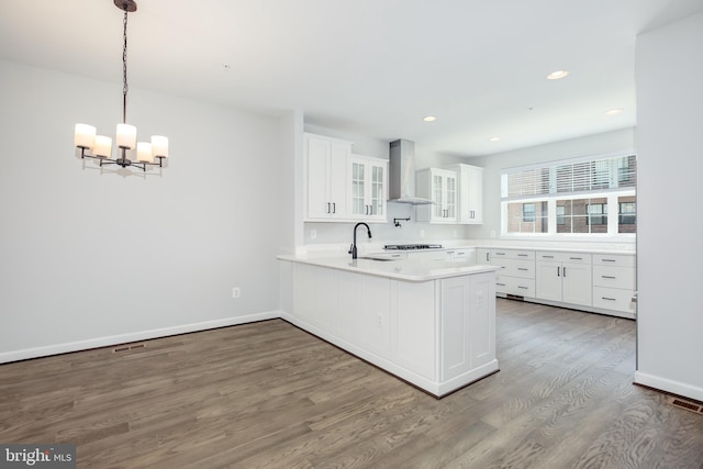 kitchen featuring white cabinetry, hanging light fixtures, wall chimney range hood, dark hardwood / wood-style floors, and kitchen peninsula