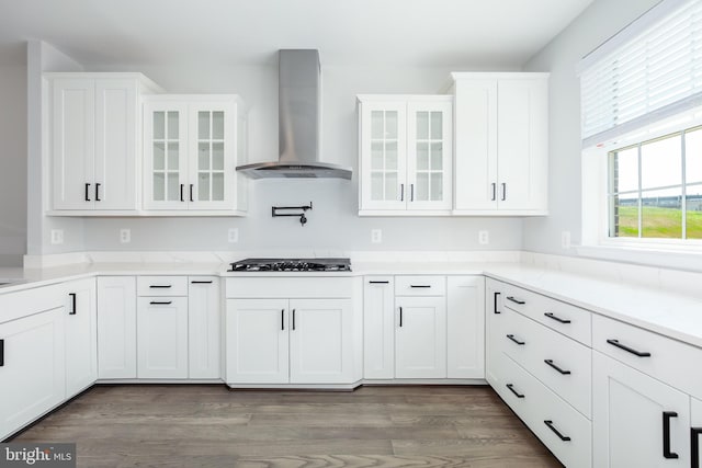 kitchen with white cabinets, gas stovetop, wall chimney range hood, and hardwood / wood-style flooring