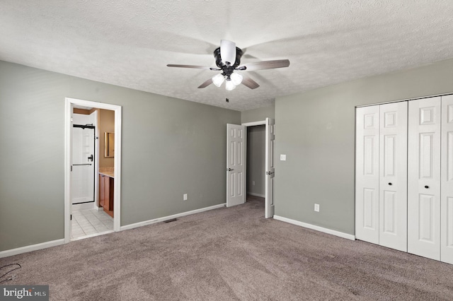 unfurnished bedroom with ensuite bath, a textured ceiling, a closet, light colored carpet, and ceiling fan