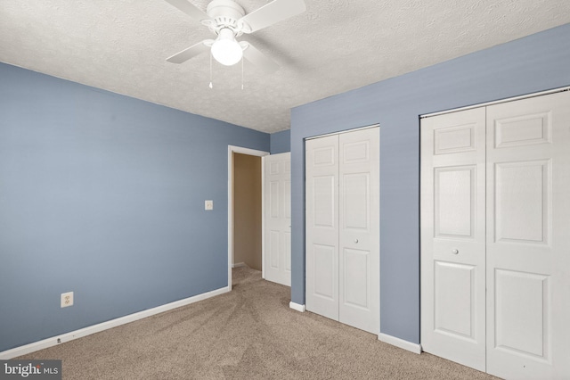 unfurnished bedroom featuring ceiling fan, multiple closets, carpet, and a textured ceiling