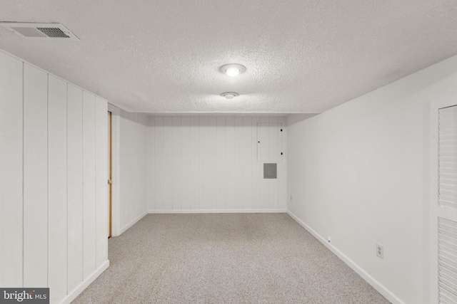 basement featuring a textured ceiling, light carpet, and wood walls