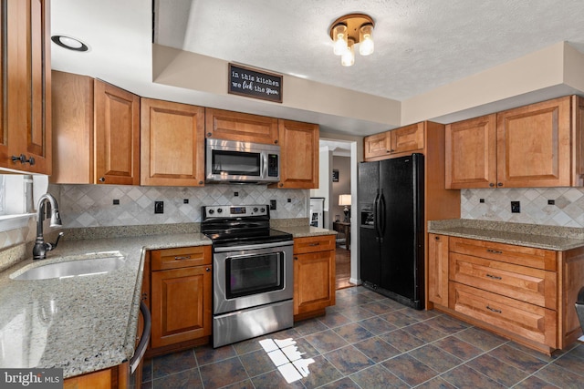 kitchen with stainless steel appliances, light stone countertops, a textured ceiling, decorative backsplash, and sink