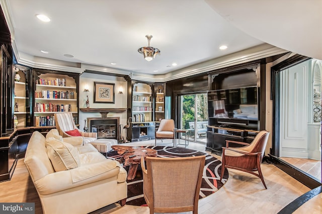 sitting room with light wood-type flooring, built in features, and crown molding