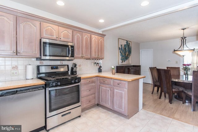 kitchen with tasteful backsplash, tile countertops, hanging light fixtures, kitchen peninsula, and stainless steel appliances