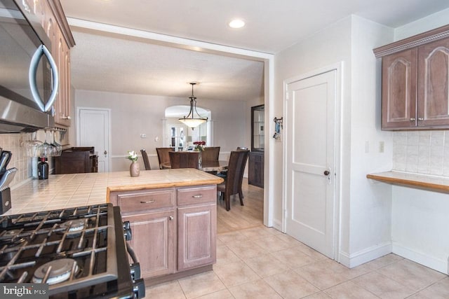 kitchen featuring hanging light fixtures, light tile patterned flooring, tile countertops, and backsplash