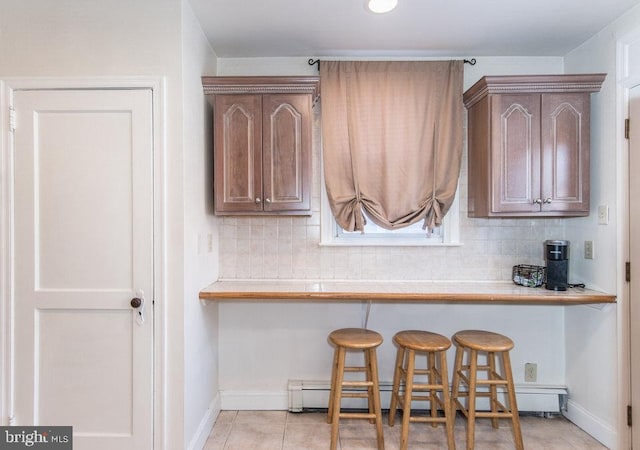 kitchen featuring a baseboard heating unit, decorative backsplash, a kitchen breakfast bar, and light tile patterned floors