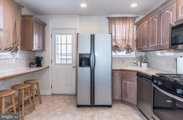 kitchen featuring tasteful backsplash, sink, tile counters, light tile patterned floors, and stainless steel appliances