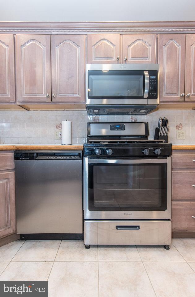 kitchen featuring tile countertops, appliances with stainless steel finishes, light tile patterned floors, and decorative backsplash