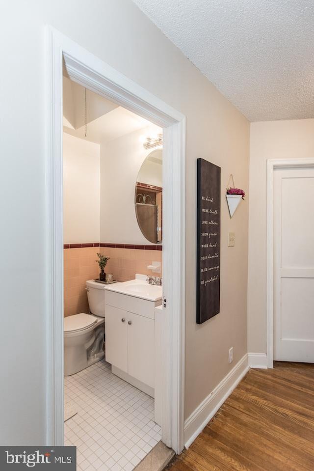 bathroom featuring tile walls, vanity, wood-type flooring, a textured ceiling, and toilet