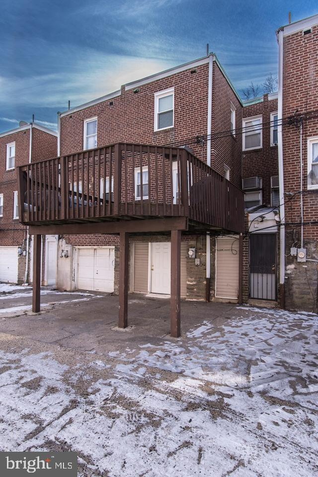 snow covered back of property featuring a garage and a wooden deck