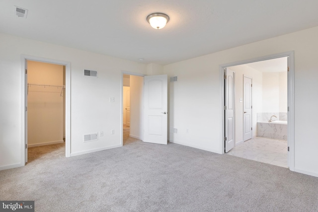 unfurnished bedroom with a spacious closet, a closet, ensuite bathroom, and light carpet