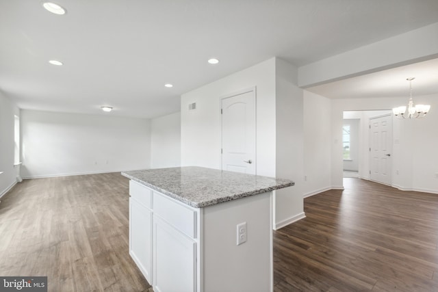 kitchen featuring light stone countertops, a kitchen island, a notable chandelier, white cabinetry, and hanging light fixtures