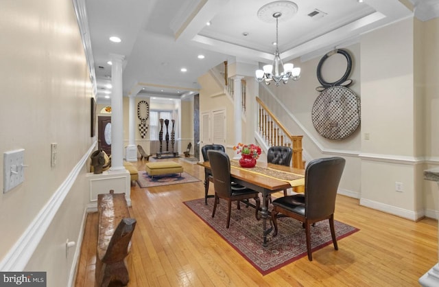 dining room with decorative columns, a raised ceiling, light wood-type flooring, ornamental molding, and a chandelier