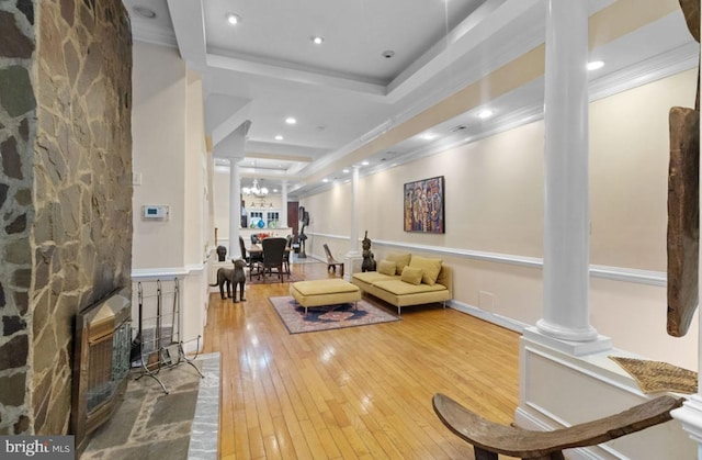 living room with ornate columns, a raised ceiling, a notable chandelier, hardwood / wood-style flooring, and crown molding