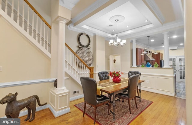 dining room with a raised ceiling, crown molding, a chandelier, and light wood-type flooring