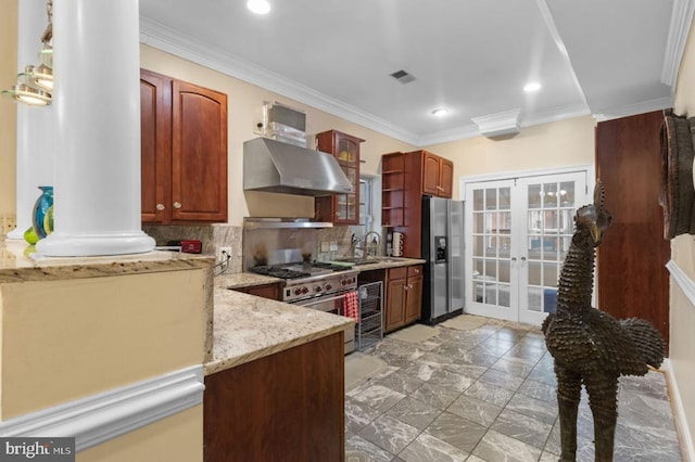 kitchen featuring light stone countertops, wall chimney exhaust hood, stainless steel appliances, french doors, and decorative backsplash