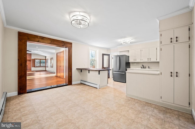 kitchen with a baseboard heating unit, kitchen peninsula, stainless steel fridge, a breakfast bar area, and white cabinets