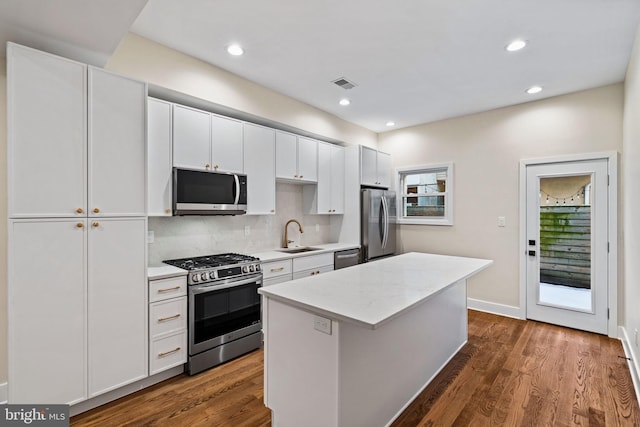 kitchen featuring appliances with stainless steel finishes, sink, white cabinets, a center island, and dark wood-type flooring