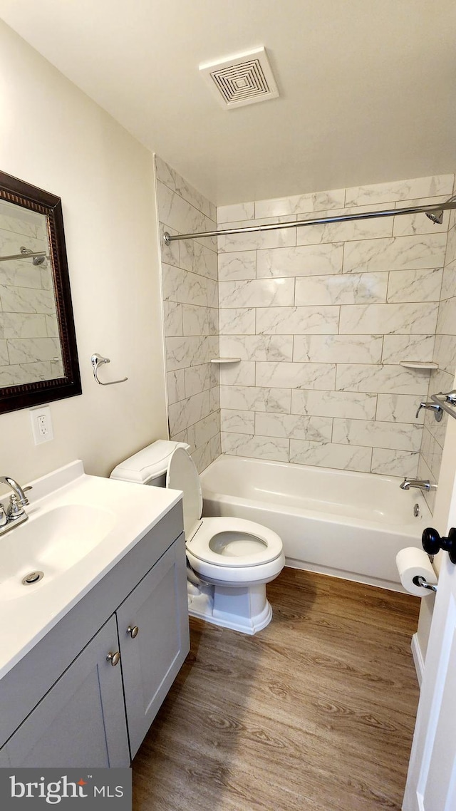 full bathroom with tiled shower / bath, vanity, wood-type flooring, and toilet